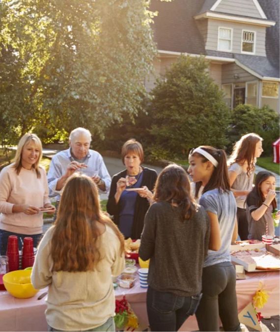 a group of people standing around a picnic table eating and smiling