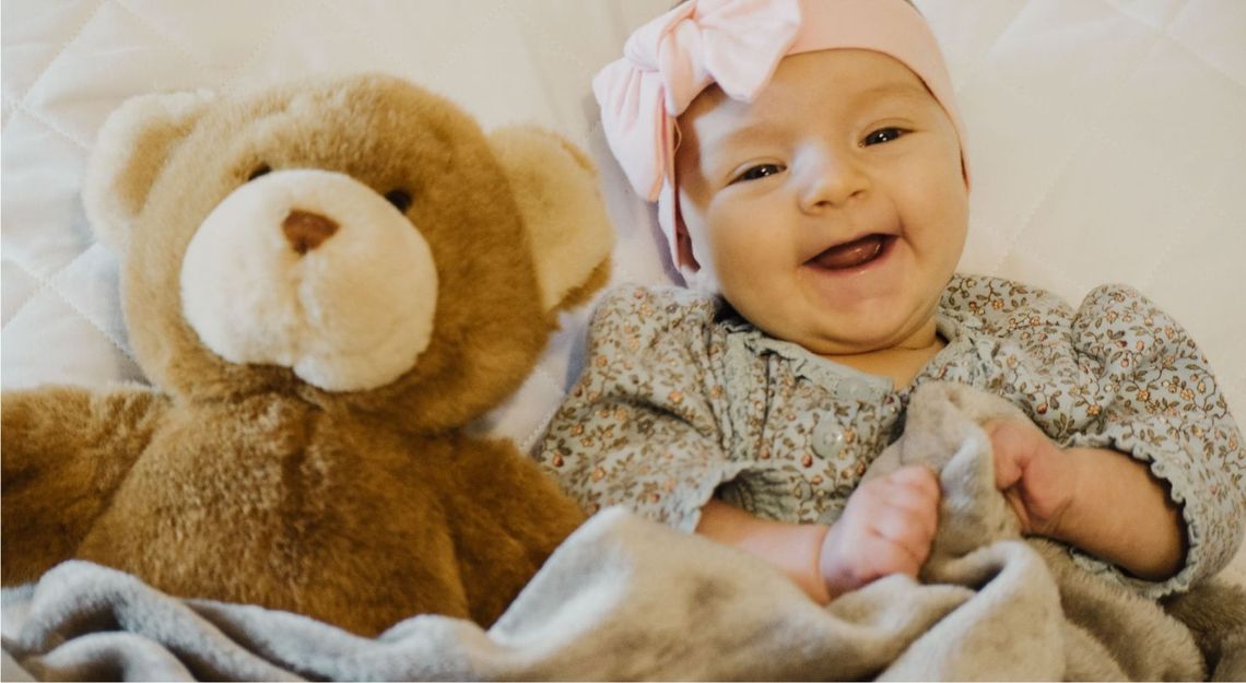 A smiling child tucked in with their teddy bear